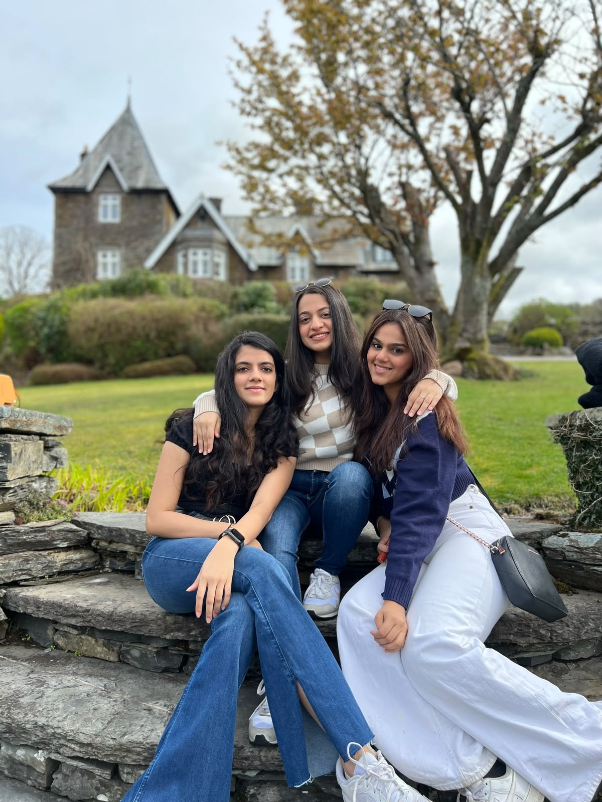 Three friends seated together on stone steps in a scenic countryside setting