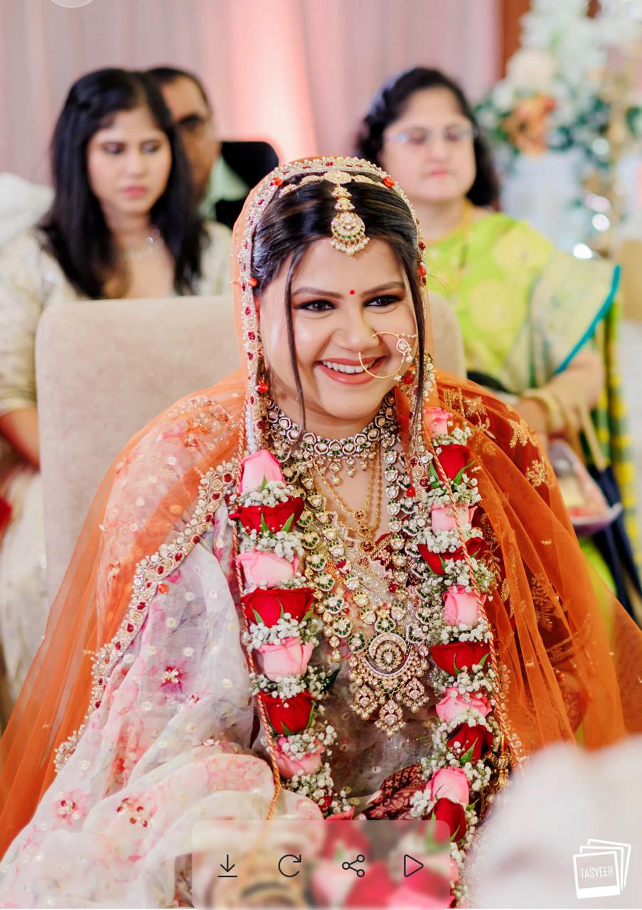 Bride in an ornate floral lehenga with an orange dupatta and rose garland