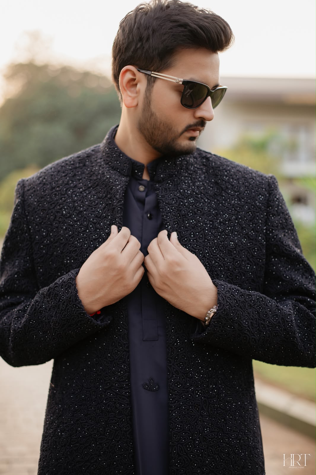 Groom in a dark embroidered sherwani adjusting his collar